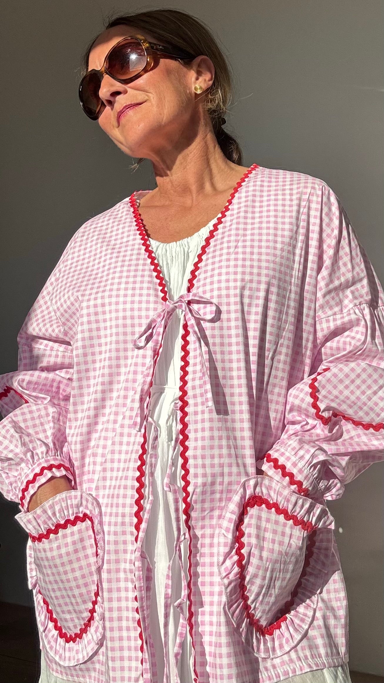 Rosa-weiß kariertes Baumwolljäckchen mit überschnittenen Schultern, Puffärmeln, roten Herzstickereien auf Ärmeln und herzförmigen Taschen. Schleifenverschluss vorn. Rückenlänge ca. 65 cm, passend für Größen 34–42