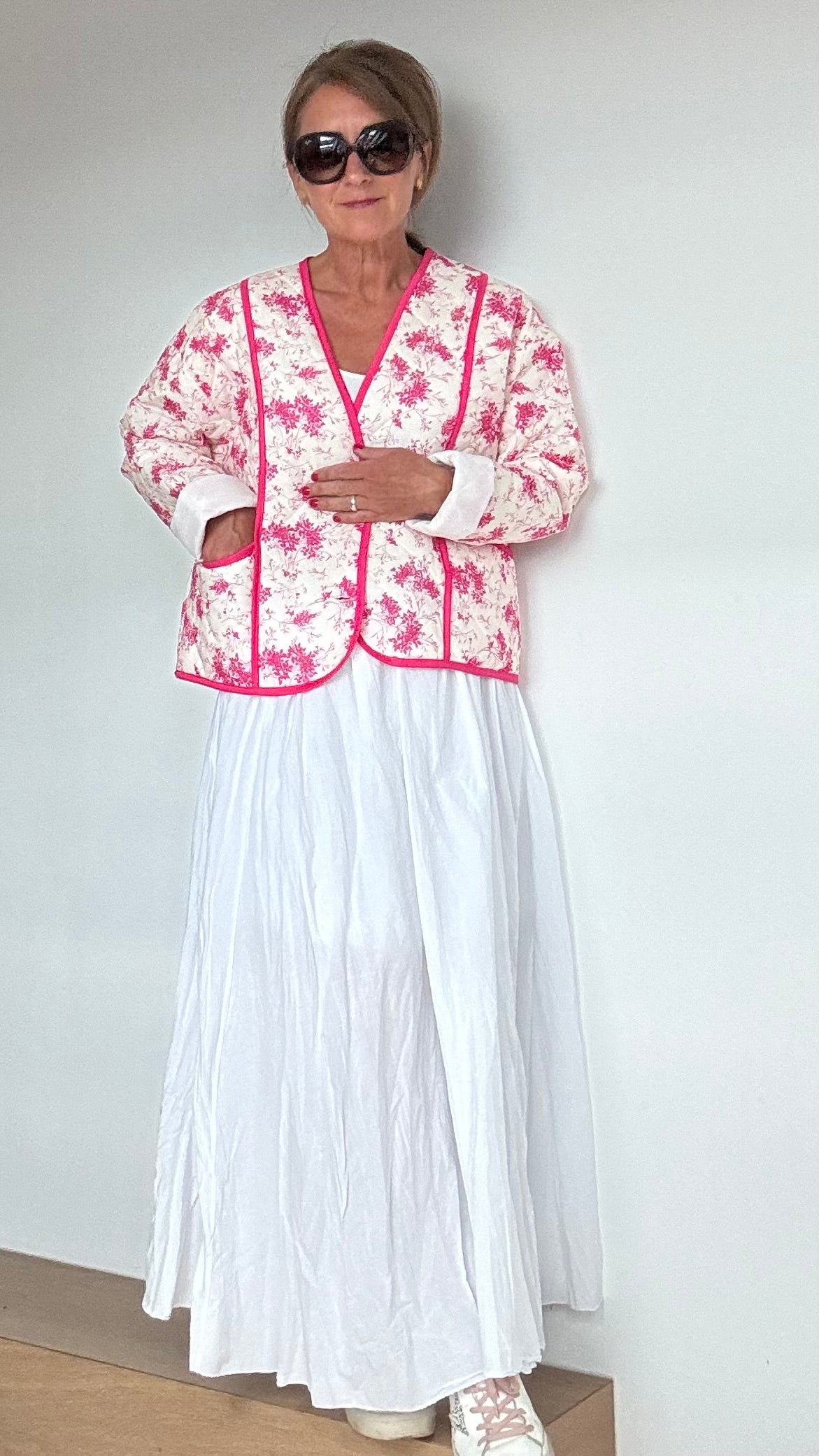 Steppjacke aus 100% Baumwolle in strahlendem Weiß mit pinkem Blumenmuster. Die Jacke kann offen oder mit eleganten Knöpfen geschlossen getragen werden. Mit einem oversized Schnitt und einer Rückenlänge von 56 cm passt sie perfekt über weite Kleider oder Röcke. Besondere Details sind aufgesetzte Taschen und feine Ziernähte. Ideal für kühlere Tage und bietet hohen Tragekomfort.