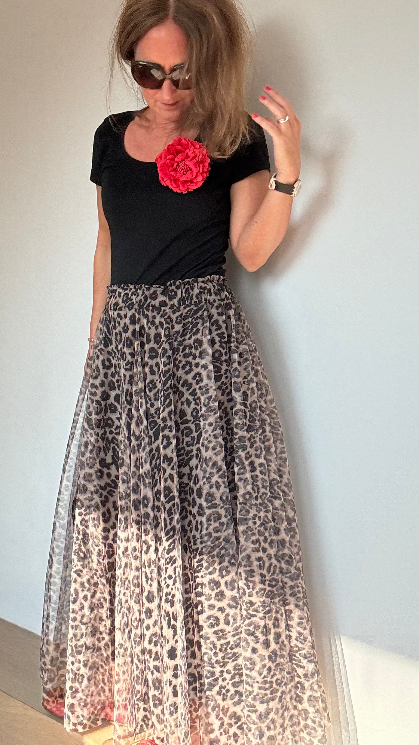 Frau trägt ein schwarzes T-shirt mit einer roten Bluembrosche, dazu den Tüllrock in der Farbvariante heller Leo-Print. Details findest du in unserer Produktbeschreibung.