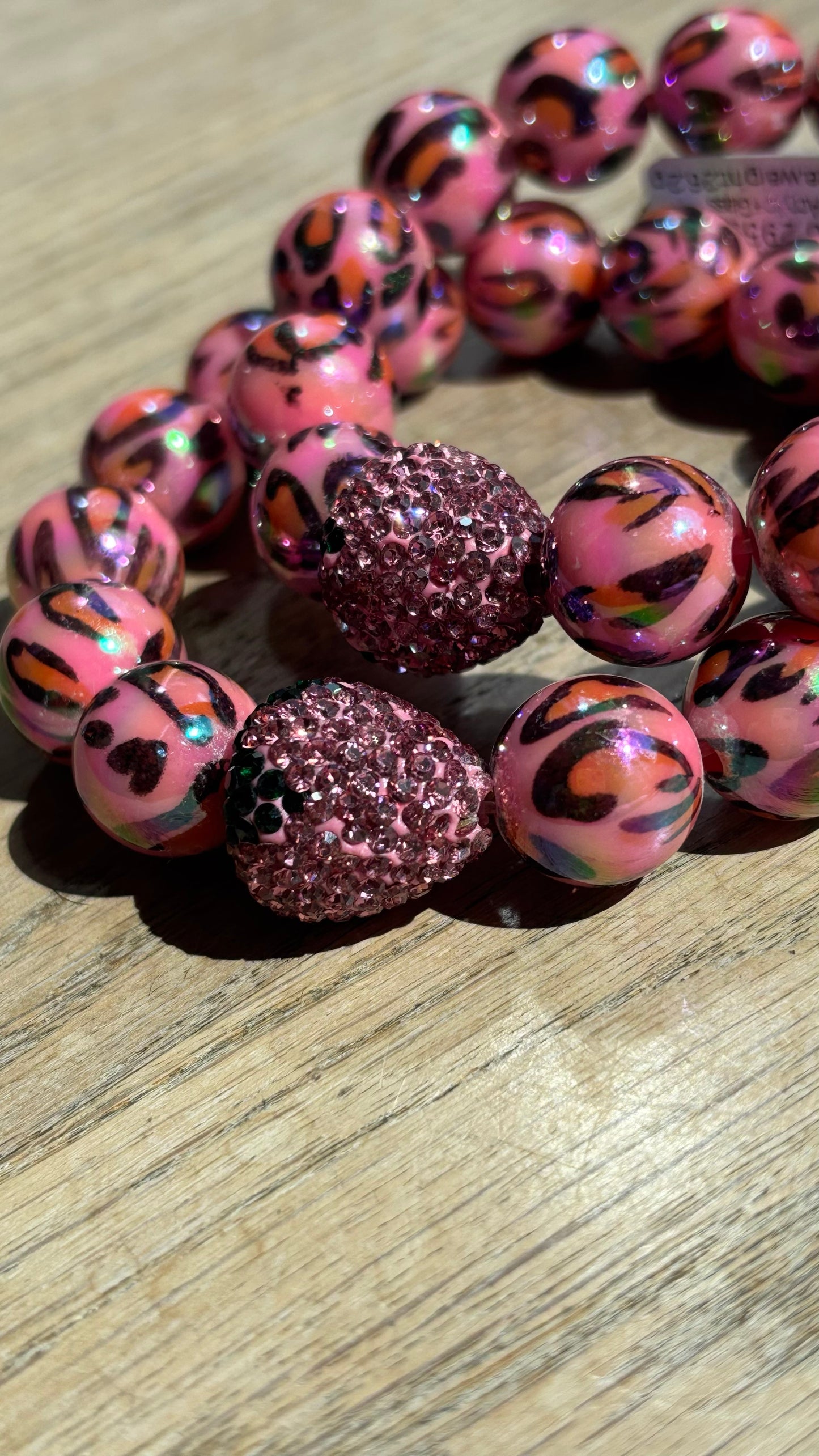 Verspieltes Perlenarmband mit auffälligen rosa Leo-Print-Perlen und einer glitzernden rosa Strass-Erdbeere als Eyecatcher. Das Armband liegt auf hellem Untergrund und kombiniert wilden Animal-Print mit sommerlicher Leichtigkeit – ideal für trendige Sommer-Looks.