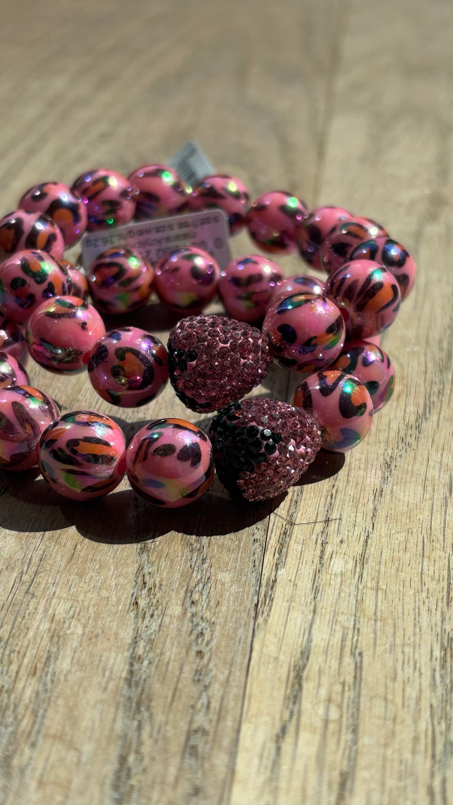 Verspieltes Perlenarmband mit auffälligen rosa Leo-Print-Perlen und einer glitzernden rosa Strass-Erdbeere als Eyecatcher. Das Armband liegt auf hellem Untergrund und kombiniert wilden Animal-Print mit sommerlicher Leichtigkeit – ideal für trendige Sommer-Looks.