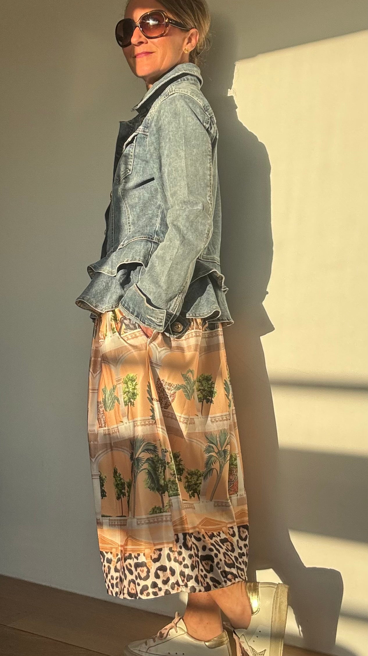 Statement-Midirock 'Lost Paradise' mit exotischem Muster: Tiger, Elefanten, Tukane und Palmen blicken aus kunstvollen Rundbögen hervor, inspiriert von historischen Zoologiegärten. Der Rock ist in elegante Kellerfalten gelegt, hat Eingriffstaschen und ein elastisches Bündchen am Rücken für Komfort. Der Saumabschluss setzt mit einem Leo-Muster ein zusätzliches Highlight. Perfekt für stilvolle Looks mit engen Tops, Cardigans oder Jeansjacken – kombinierbar mit Sneakern oder Ballerinas