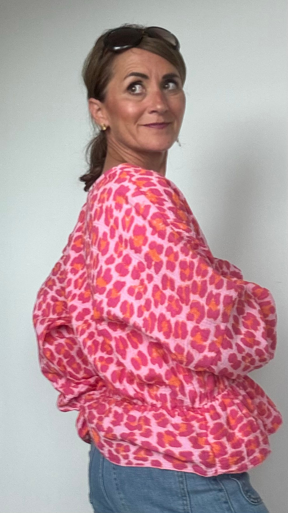 Sommerliche Wickelbluse aus pinkfarbenem Musselin mit Leoprint, Puffärmeln in Fledermausform und kurzem Rüschenschößchen. Seitlich mit Schleife bindbar, innenliegendes elastisches Bündchen für sicheren Sitz. Länge 55 cm, Achsel zu Achsel 60 cm. Locker geschnitten für Größen 34–42, ideal kombinierbar mit Jeans, Rock oder als Überwurf über ein Kleid.