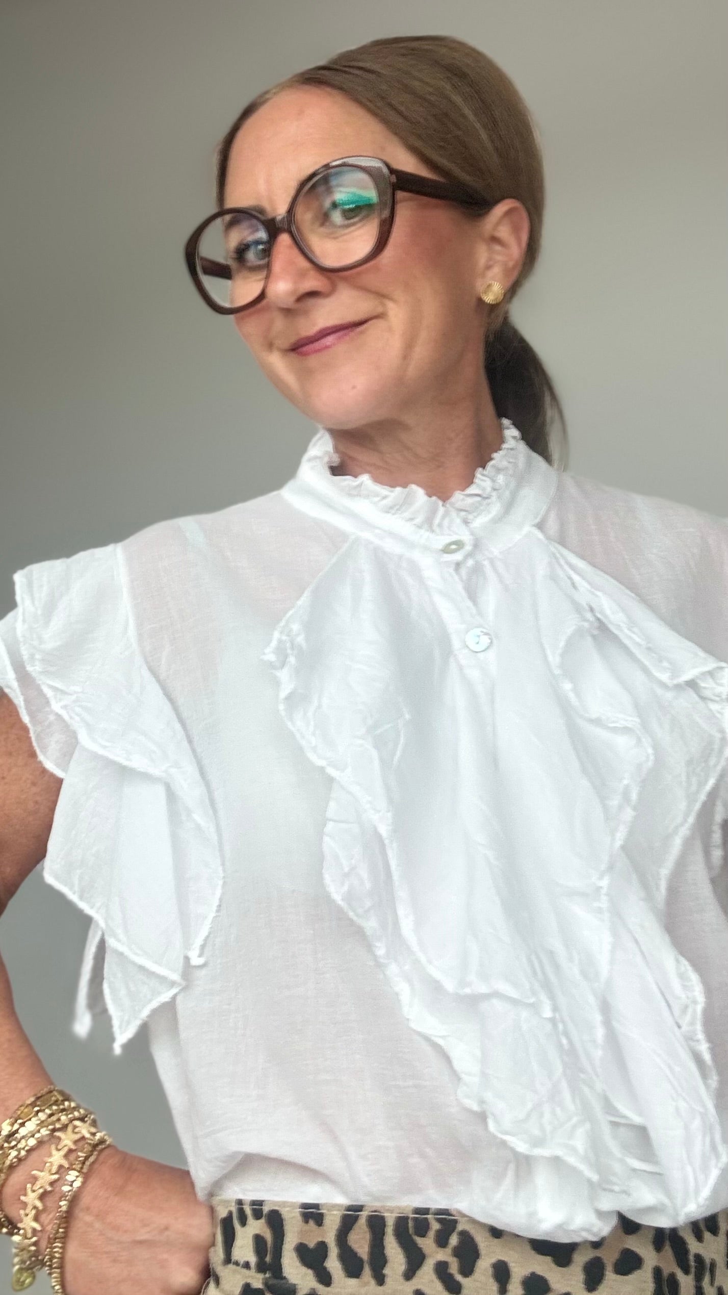 Ärmellose Bluse aus 100 % Baumwolle in zartem Weiss mit feinen Details: Wasserfallartige Volants zieren die Knopfleiste sowie die leichten Volant-Ärmel. Die Bluse hat einen kleinen Stehkragen mit Rüschen, ist gerade geschnitten und etwa 62 cm lang. Locker und stilvoll kombiniert mit Jeans und Taillengürtel oder elegant mit Rock oder Blazer tragbar – ideal für feminine Looks mit Statement-Charakter.