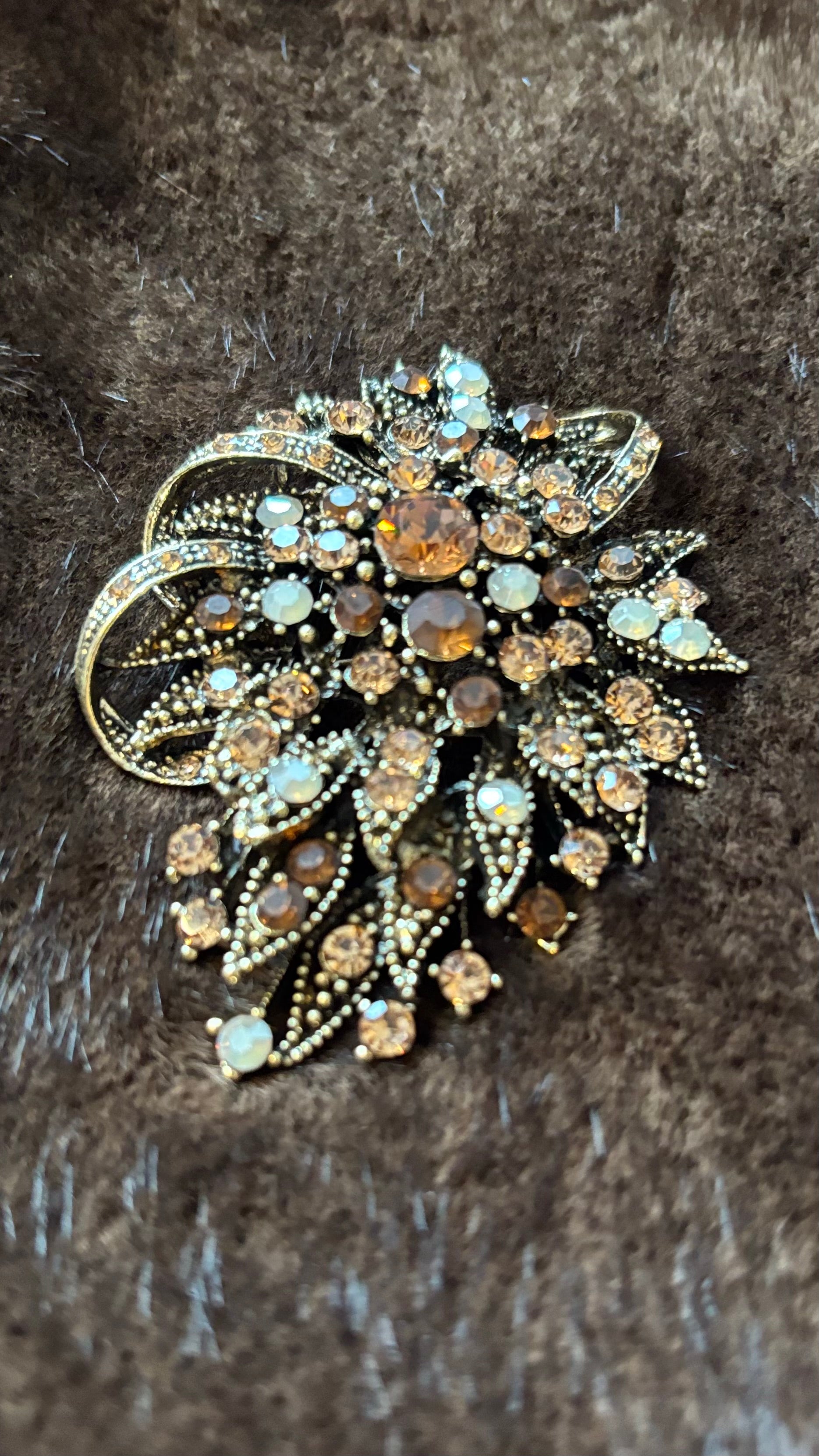 Oval-längliche Brosche mit bernsteinfarbenen, champagnerfarbenen und opalfarbenen Kristallsteinen auf goldener Metallfassung, fotografiert auf braunem Faux-Fur.