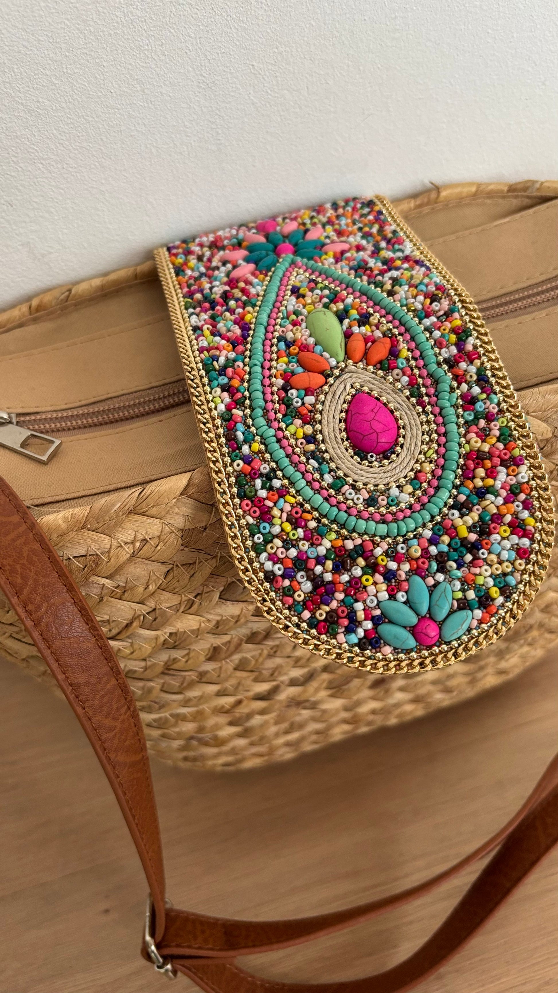 Boho-Umhängetasche aus geflochtenem Korb mit verstellbarem Schulterriemen. Die Schnalle ist kunstvoll mit Perlen- und Steinbesatz verziert. Die Tasche ist mit beigem Stoff gefüttert, hat ein kleines Innenfach und lässt sich mit einem Reißverschluss sicher schließen. Kompakte Größe mit genügend Platz für die wichtigsten Essentials – perfekt für den Alltag oder besondere Anlässe.
