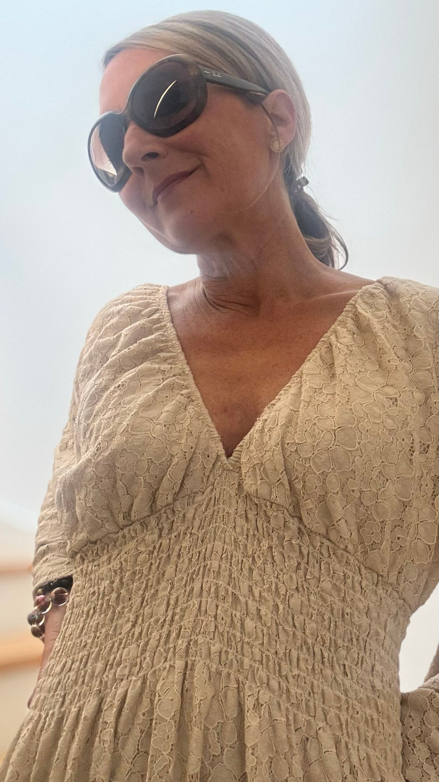 Beiges, langes Kleid mit strukturierter Oberfläche in Spitze-Optik, gesmoktem Einsatz unter der Brust und trompetenförmigen Ärmeln. Locker fallendes Maxikleid mit Volant am Saum, unterfüttert und kombiniert mit braunen Boots.