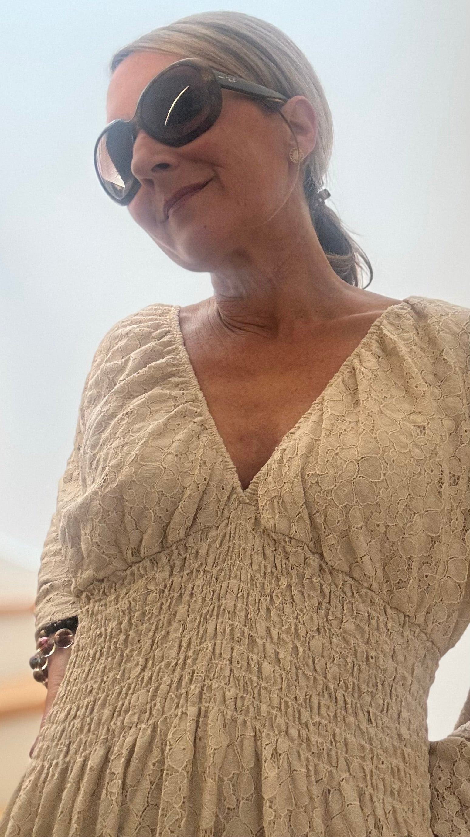 Beiges, langes Kleid mit strukturierter Oberfläche in Spitze-Optik, gesmoktem Einsatz unter der Brust und trompetenförmigen Ärmeln. Locker fallendes Maxikleid mit Volant am Saum, unterfüttert und kombiniert mit braunen Boots.