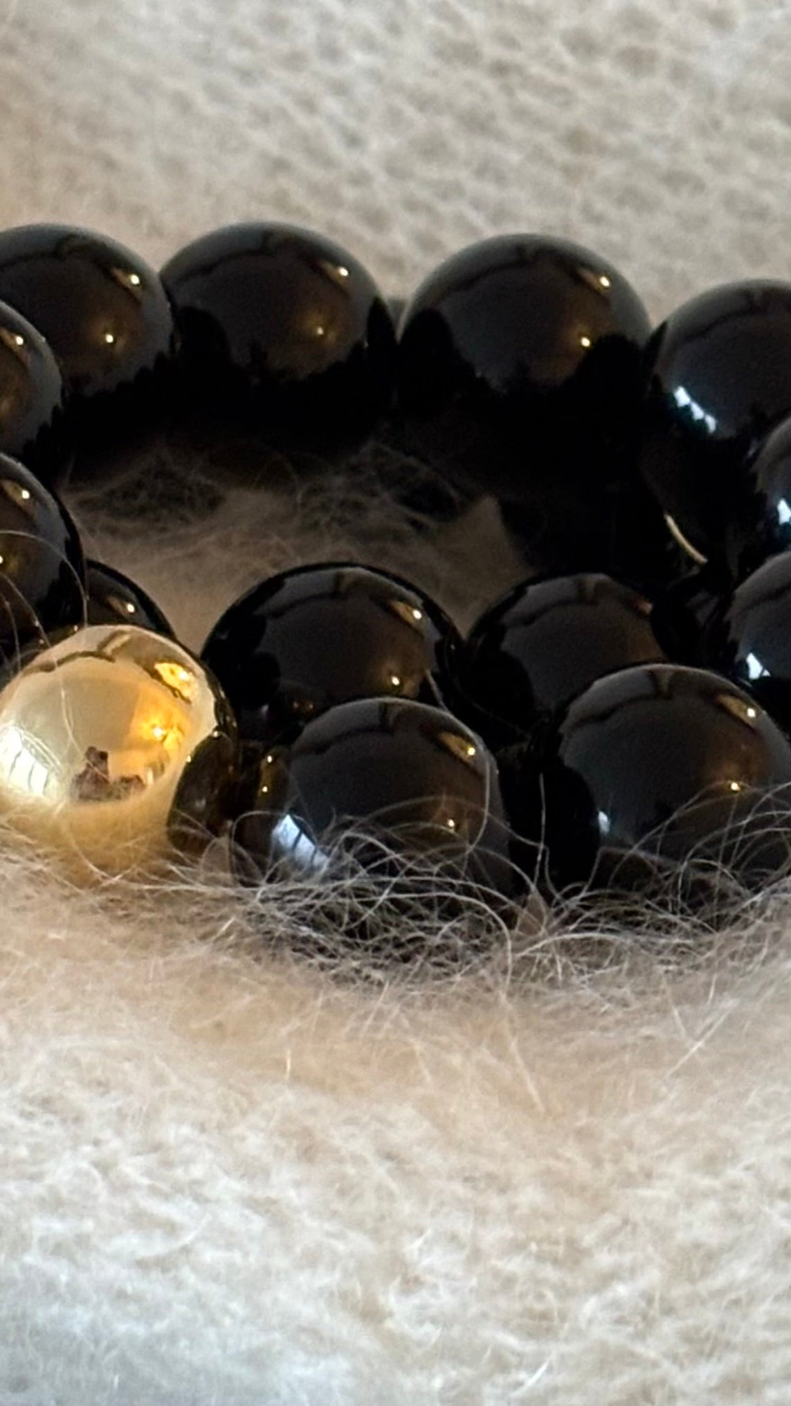 Schwarzes Perlenarmband mit großen 20-mm-Perlen und einer goldenen Akzentperle. Glatte, glänzende Oberfläche auf hellem Hintergrund.