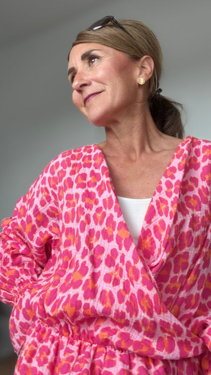 Sommerliche Wickelbluse aus pinkfarbenem Musselin mit Leoprint, Puffärmeln in Fledermausform und kurzem Rüschenschößchen. Seitlich mit Schleife bindbar, innenliegendes elastisches Bündchen für sicheren Sitz. Länge 55 cm, Achsel zu Achsel 60 cm. Locker geschnitten für Größen 34–42, ideal kombinierbar mit Jeans, Rock oder als Überwurf über ein Kleid.

