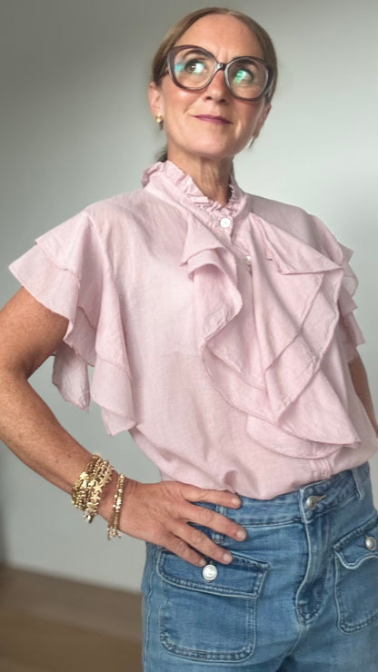 Ärmellose Bluse aus 100 % Baumwolle in zartem Altrosa mit feinen Details: Wasserfallartige Volants zieren die Knopfleiste sowie die leichten Volant-Ärmel. Die Bluse hat einen kleinen Stehkragen mit Rüschen, ist gerade geschnitten und etwa 62 cm lang. Locker und stilvoll kombiniert mit Jeans und Taillengürtel oder elegant mit Rock oder Blazer tragbar – ideal für feminine Looks mit Statement-Charakter.


