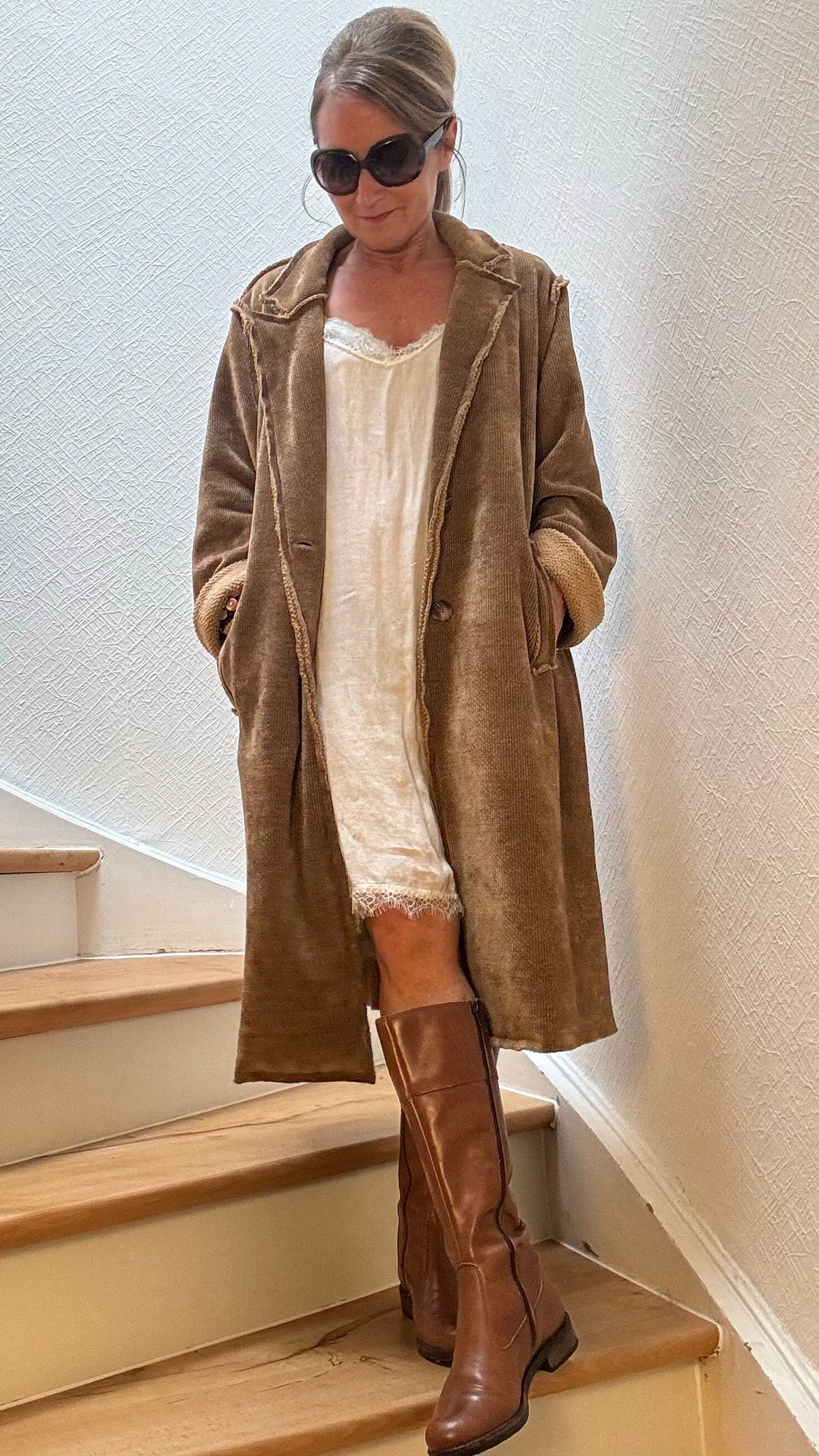 Retro Mood Cord Coat in Cognac aus breitem Niki-Cord, kombiniert mit hellem Spitzenkleid und braunen Stiefeln
