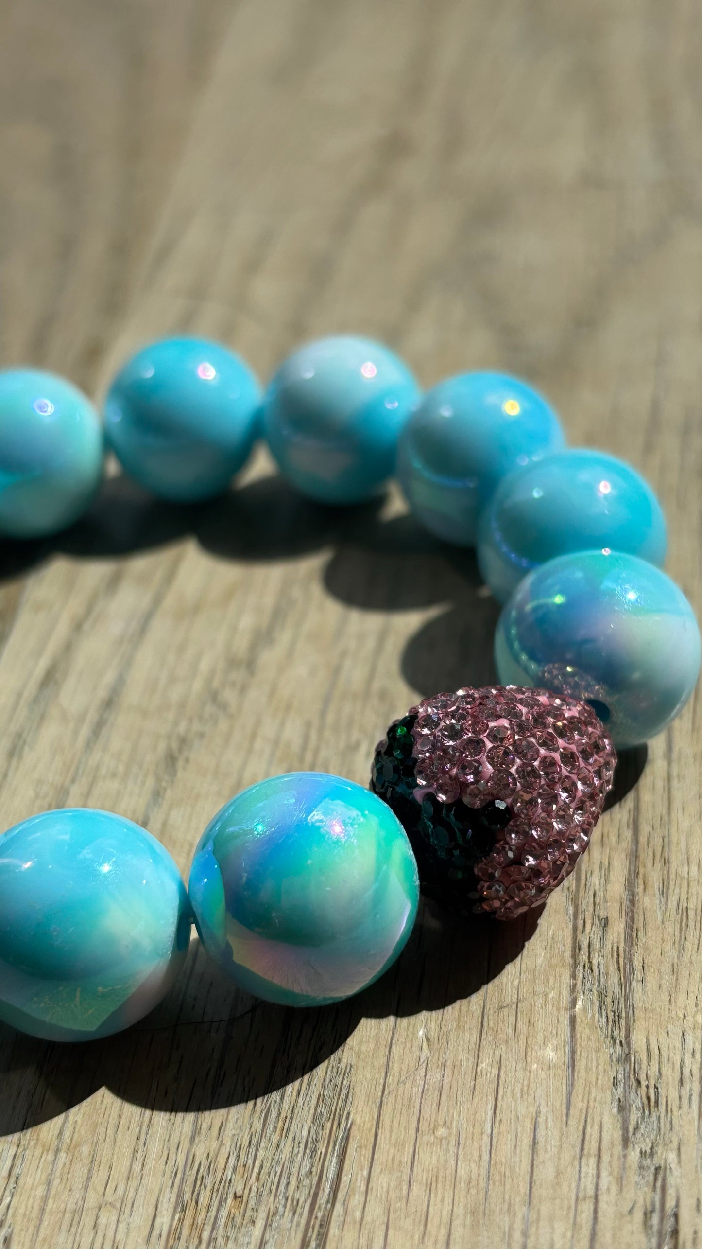 Perlenarmband Erdbeerliebe mit zarten runden Perlen in Soft Gelb bzw. Hellblau. Highlight ist eine kleine, funkelnde Strass-Erdbeere als Schmuckelement. Das Armband liegt auf einem weißen Hintergrund und wirkt verspielt und sommerlich. Ideal als Accessoire für Frühling und Sommer.