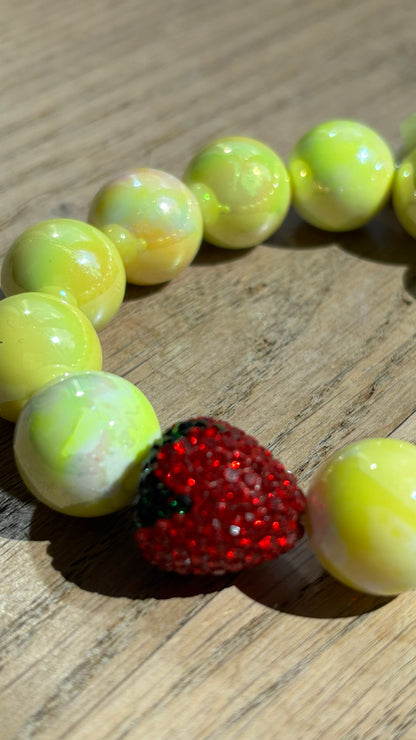 Perlenarmband Erdbeerliebe mit zarten runden Perlen in Soft Gelb bzw. Hellblau. Highlight ist eine kleine, funkelnde Strass-Erdbeere als Schmuckelement. Das Armband liegt auf einem weißen Hintergrund und wirkt verspielt und sommerlich. Ideal als Accessoire für Frühling und Sommer.