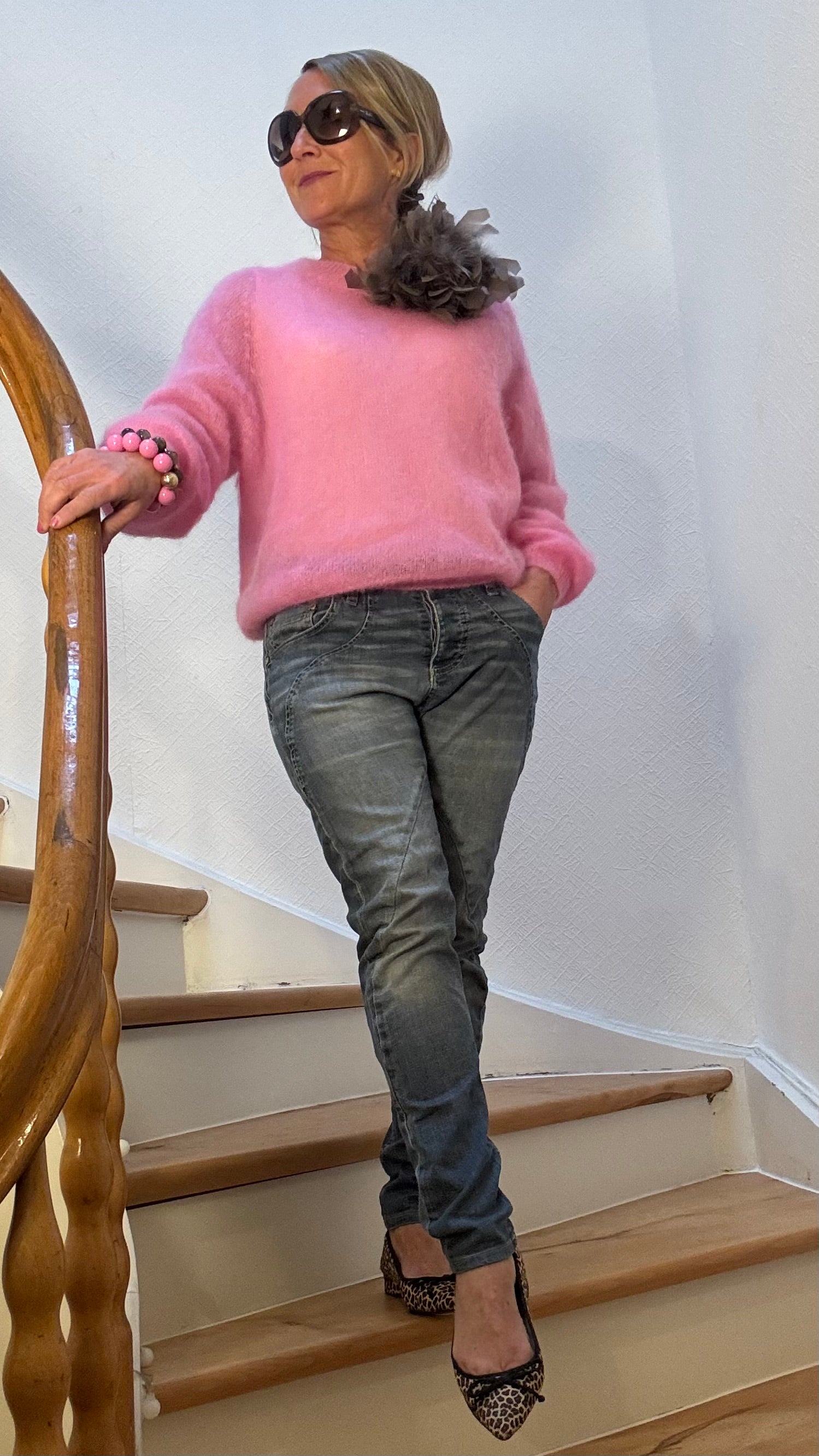 Pullover aus feinem Kid-Mohair in zartem Rosa mit Rundhalsausschnitt, kombiniert mit Jeans und Federbrosche.
