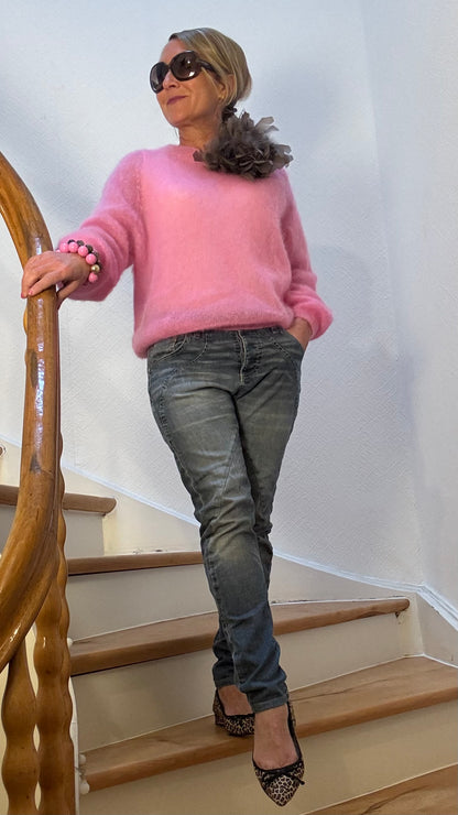 Pullover aus feinem Kid-Mohair in zartem Rosa mit Rundhalsausschnitt, kombiniert mit Jeans und Federbrosche.
