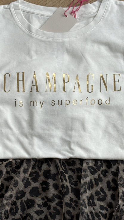 Cremeweißes T-Shirt mit einem lockeren Halsausschnitt und kurzen Ärmeln, auf der Brust steht in Pink geschreiben: Champagne is my superfood. Details findest du in unserer Produktbeschreibung.
