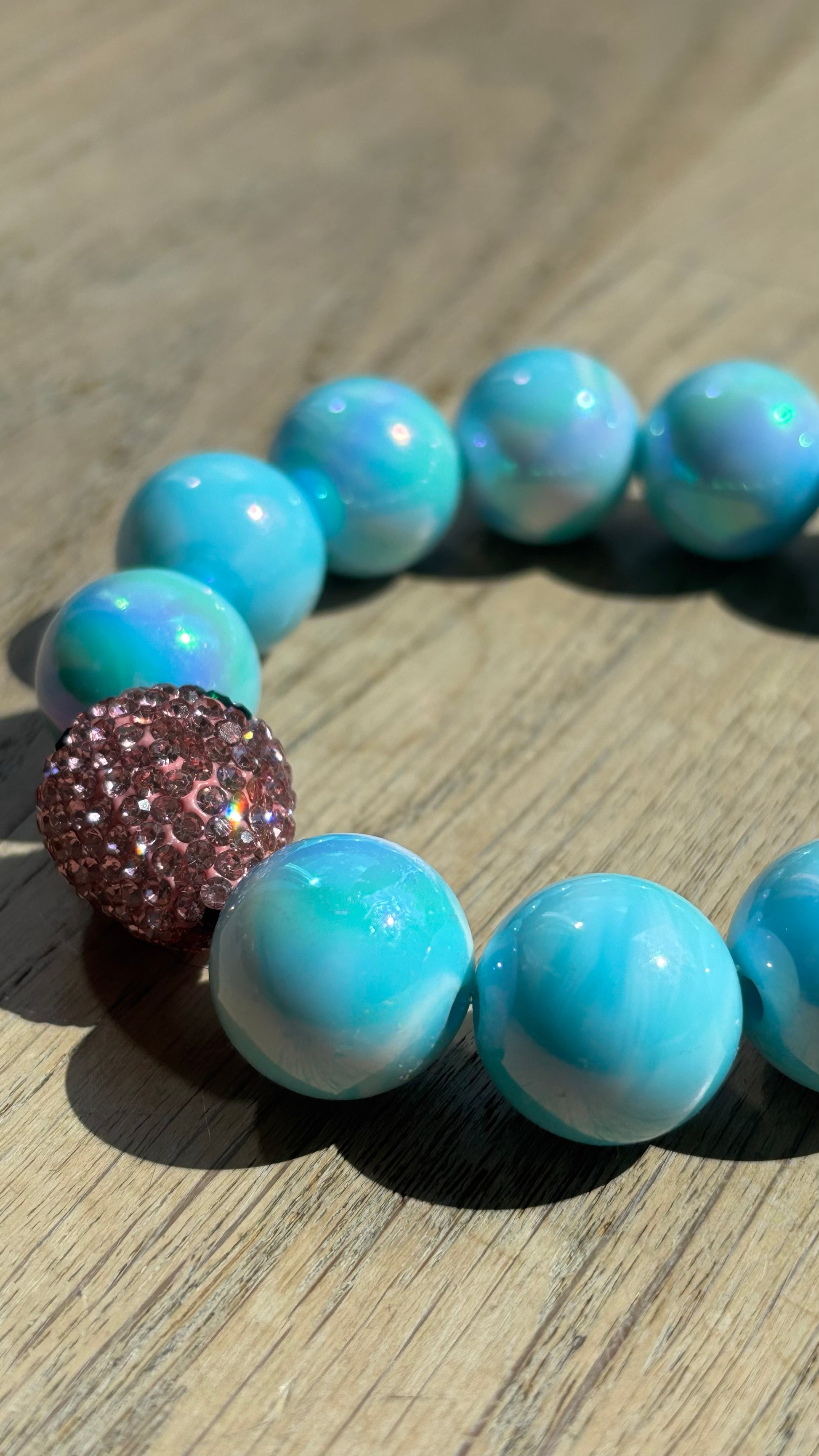 Perlenarmband Erdbeerliebe mit zarten runden Perlen in Soft Gelb bzw. Hellblau. Highlight ist eine kleine, funkelnde Strass-Erdbeere als Schmuckelement. Das Armband liegt auf einem weißen Hintergrund und wirkt verspielt und sommerlich. Ideal als Accessoire für Frühling und Sommer.