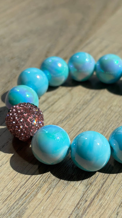 Perlenarmband Erdbeerliebe mit zarten runden Perlen in Soft Gelb bzw. Hellblau. Highlight ist eine kleine, funkelnde Strass-Erdbeere als Schmuckelement. Das Armband liegt auf einem weißen Hintergrund und wirkt verspielt und sommerlich. Ideal als Accessoire für Frühling und Sommer.