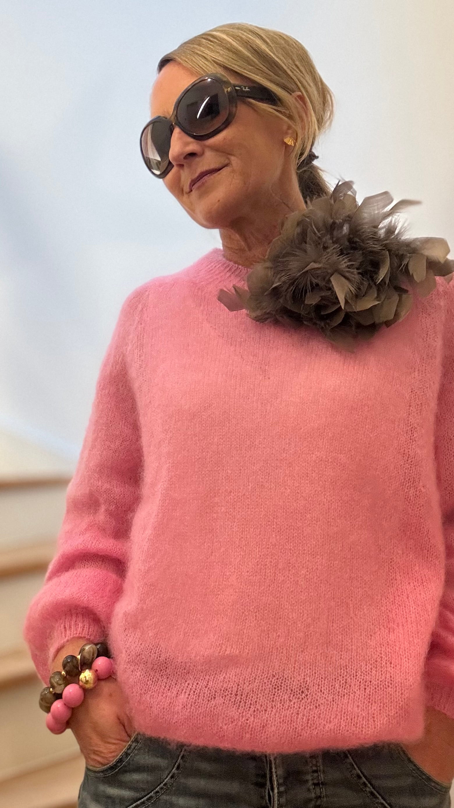 Pullover aus feinem Kid-Mohair in zartem Rosa mit Rundhalsausschnitt, kombiniert mit Jeans und Federbrosche.