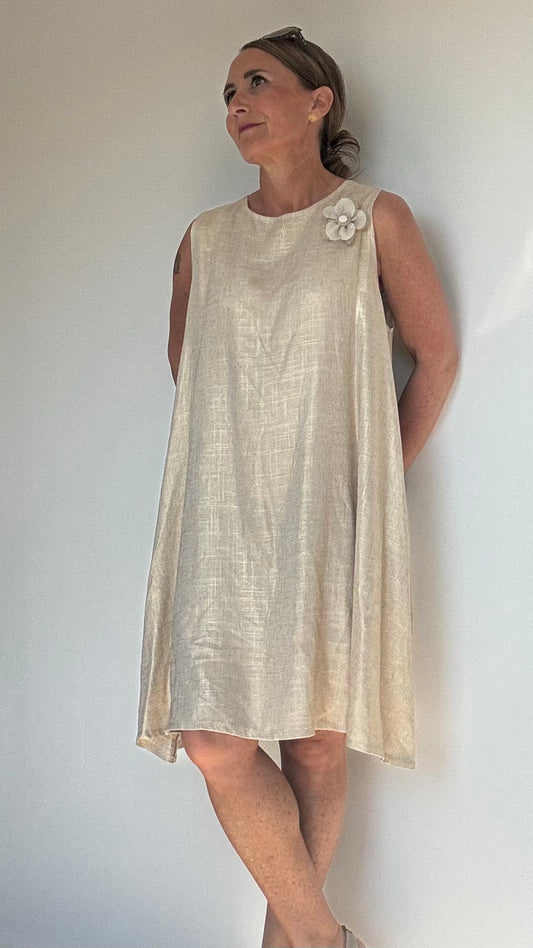Ärmelloses Sommerkleid „Golden Glow“ in edlem Goldton. A-Linien-Schnitt mit 93 cm Länge, tiefen Armausschnitten und Rundhalsausschnitt mit Knopfverschluss hinten. Hergestellt aus leichtem Rayon-Leinen-Mix. Verziert mit abnehmbarer, goldener Blumenbrosche. Passend für Größen 34–38. Ideal für elegante Sommeranlässe.