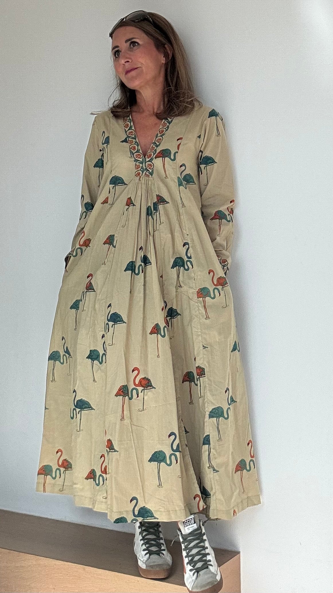 Kleid Melbourne im Tunika-Stil aus 100% Baumwolle mit V-Ausschnitt. Gesamtlänge 124 cm, Brustweite 84-86 cm, Taille 74-80 cm, Hüfte 94-98 cm. Beige mit petrol- und orangefarbenen Flamingos. Eingriffstaschen, atmungsaktiver Stoff. Ideal für Sommer, bringt Farbe in deinen Alltag