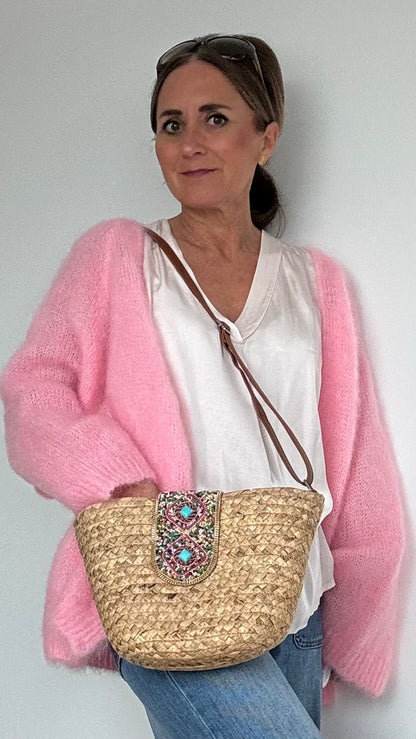 Boho-Umhängetasche aus geflochtenem Korb mit verstellbarem Schulterriemen. Die Schnalle ist kunstvoll mit Perlen- und Steinbesatz verziert. Die Tasche ist mit beigem Stoff gefüttert, hat ein kleines Innenfach und lässt sich mit einem Reißverschluss sicher schließen. Kompakte Größe mit genügend Platz für die wichtigsten Essentials – perfekt für den Alltag oder besondere Anlässe.