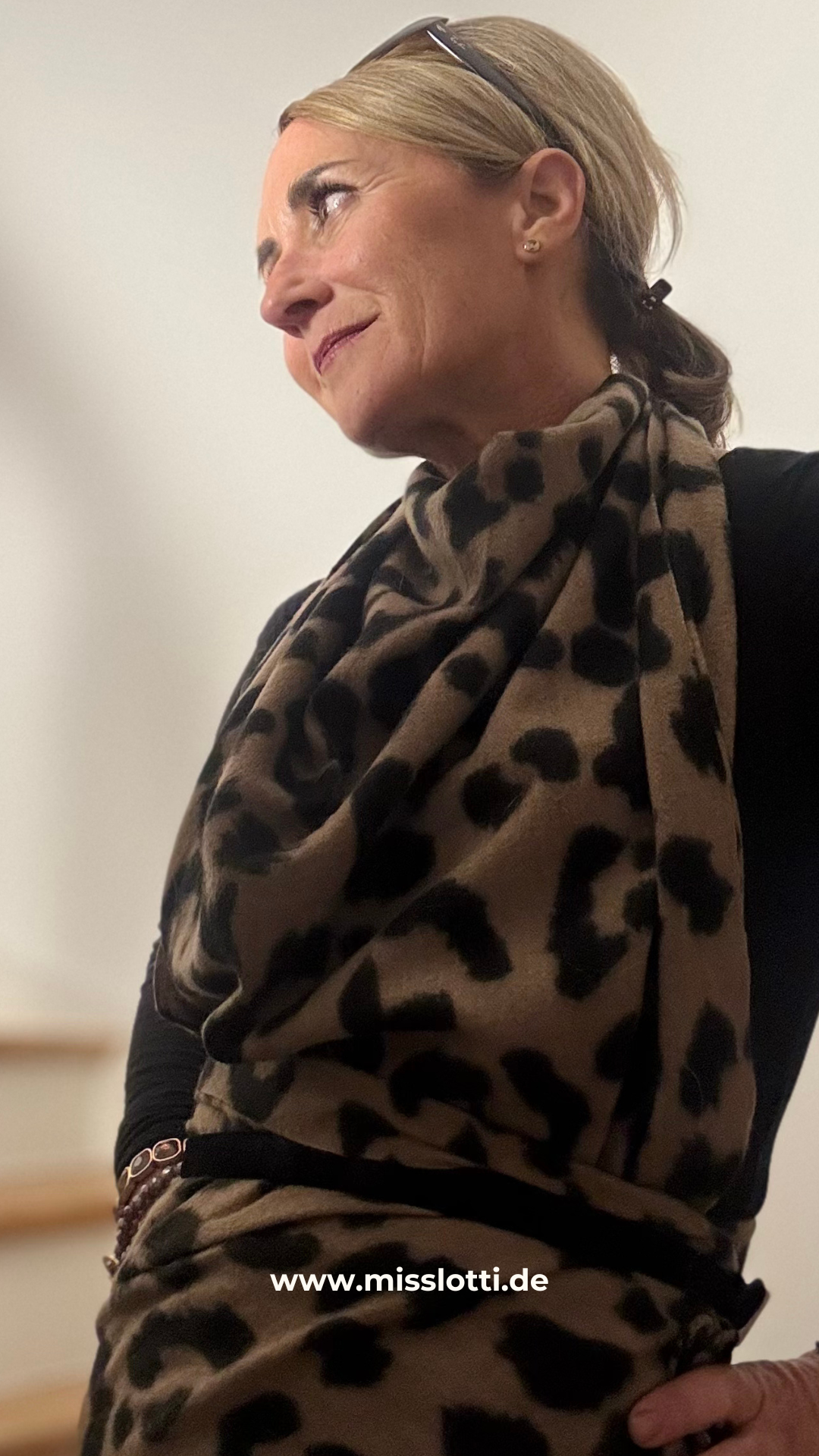 Leo Signature Schal mit klassischem Leopardenmuster, locker um den Hals getragen. Weicher Viskoseschal mit Fransen, kombiniert zu einem schwarzen Outfit.