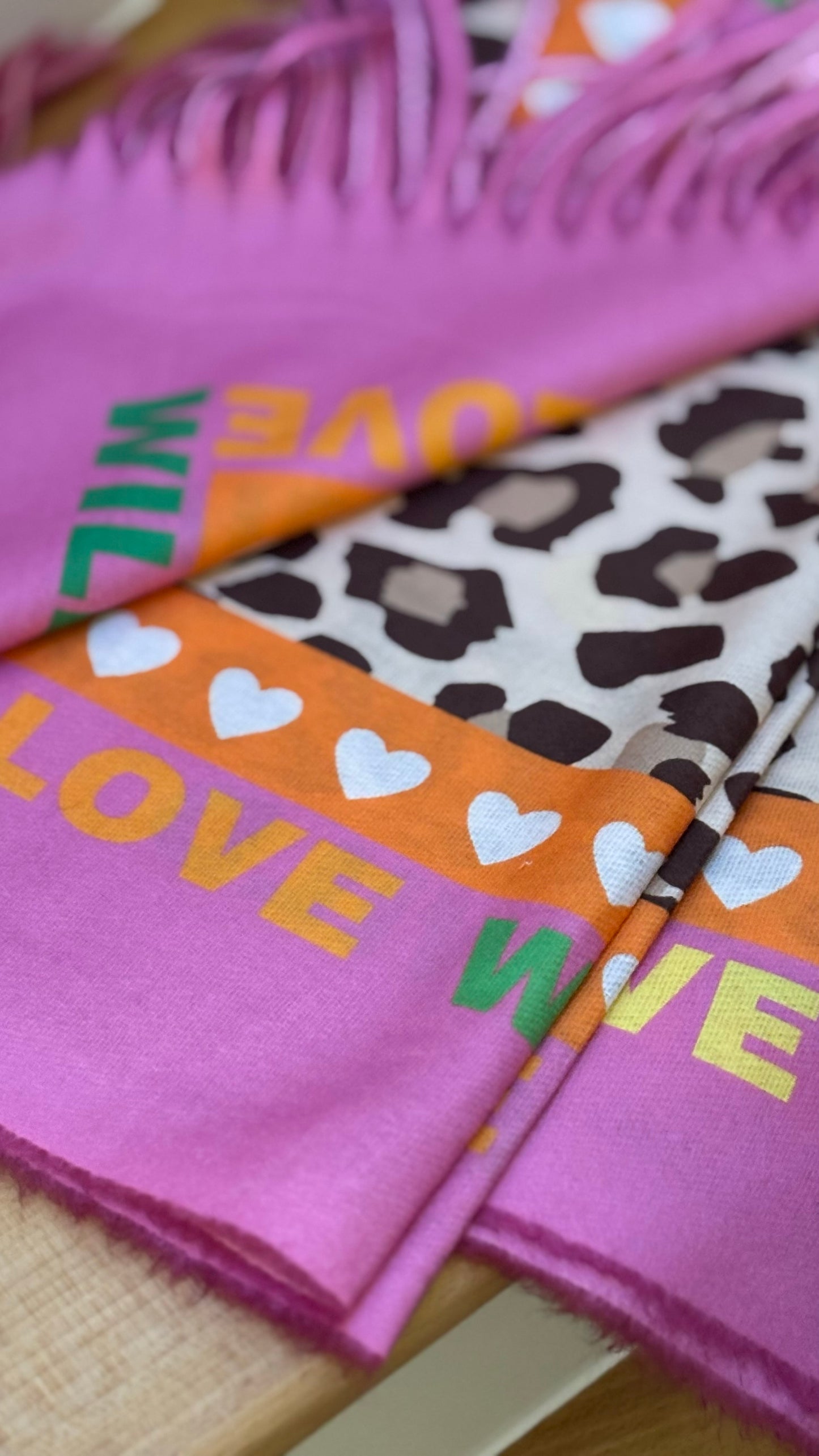 Leo-Schal in Pink und Orange mit beidseitigem Druck und Schriftzug ‚LOVE WILD‘, aus 100 % Viskose mit soften Fransen.