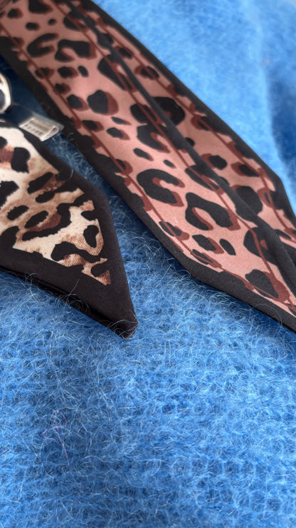 Leo-Band aus 100% Viskose, Länge 157 cm, Breite 5 cm, in hellem und dunklem Leo-Print. Spitz zulaufende Enden für vielseitige Stylingmöglichkeiten: als Halsband, Gürtel, Haarband oder Accessoire für Taschen.

