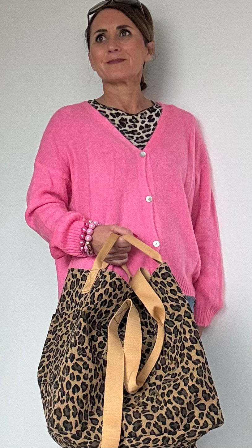 Großer Maxi-Shopper aus robustem Canvas im dunklen Leoprint mit einem goldenen Print in Form eines Smiley ohne runden Rand. Die Worte 'Happy Smile Love' formen den Umriss des Smiley-Designs. Die Tasche misst 35 cm in der Höhe, 40 cm in der Länge und 28 cm in der Breite. Innen ist die Tasche schwarz gefüttert und hat eine große Innentasche mit Reißverschluss. Zwei lange Tragegurte ermöglichen das Tragen über der Schulter, während zwei kleinere Henkel an den Seiten ein bequemes Tragen in der Hand ermöglichen.