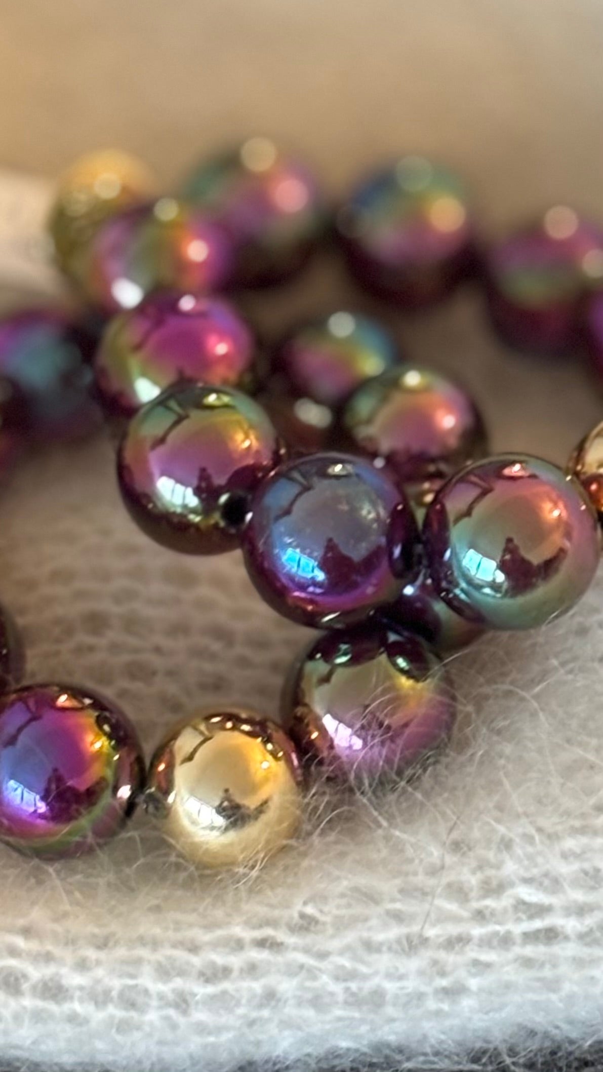 erlenarmband mit großen 20-mm-Perlen in pflaumeviolettem Beeren-Metallic und goldener Akzentperle. Opulenter, schimmernder Glow auf wollweißem Hintergrund.