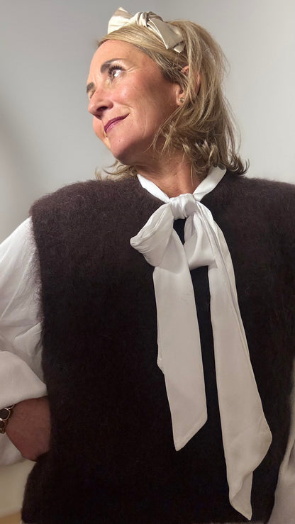 Pullunder aus Kid-Mohair in der Farbe Schoko mit klassischem Rundhalsausschnitt und tiefen Armausschnitten. Locker geschnittener, kurzer Pullunder mit weicher, flauschiger Oberfläche, ideal für Layering-Looks. Getragen über einem schlichten Outfit in warmen Naturtöne