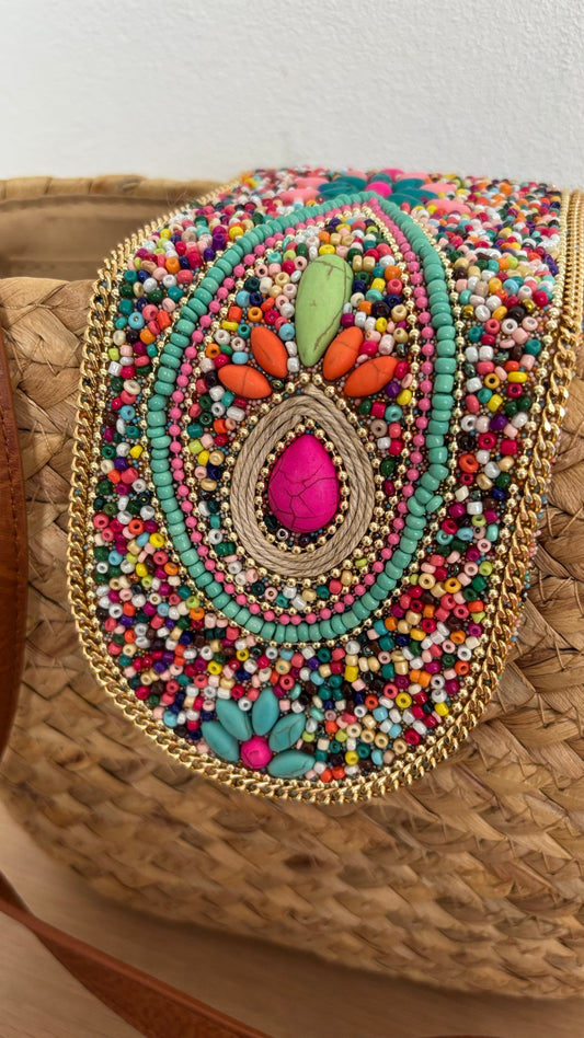 Boho-Umhängetasche aus geflochtenem Korb mit verstellbarem Schulterriemen. Die Schnalle ist kunstvoll mit Perlen- und Steinbesatz verziert. Die Tasche ist mit beigem Stoff gefüttert, hat ein kleines Innenfach und lässt sich mit einem Reißverschluss sicher schließen. Kompakte Größe mit genügend Platz für die wichtigsten Essentials – perfekt für den Alltag oder besondere Anlässe.