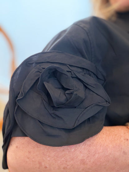 Schwarze Bluse aus Baumwolle mit verdeckter Knopfleiste und auffälligen Stoffblüten an den Ärmeln. Locker geschnitten mit überschnittenen Schultern und längerem Rückenteil.