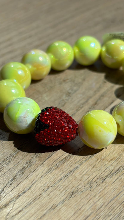 Perlenarmband Erdbeerliebe mit zarten runden Perlen in Soft Gelb bzw. Hellblau. Highlight ist eine kleine, funkelnde Strass-Erdbeere als Schmuckelement. Das Armband liegt auf einem weißen Hintergrund und wirkt verspielt und sommerlich. Ideal als Accessoire für Frühling und Sommer.