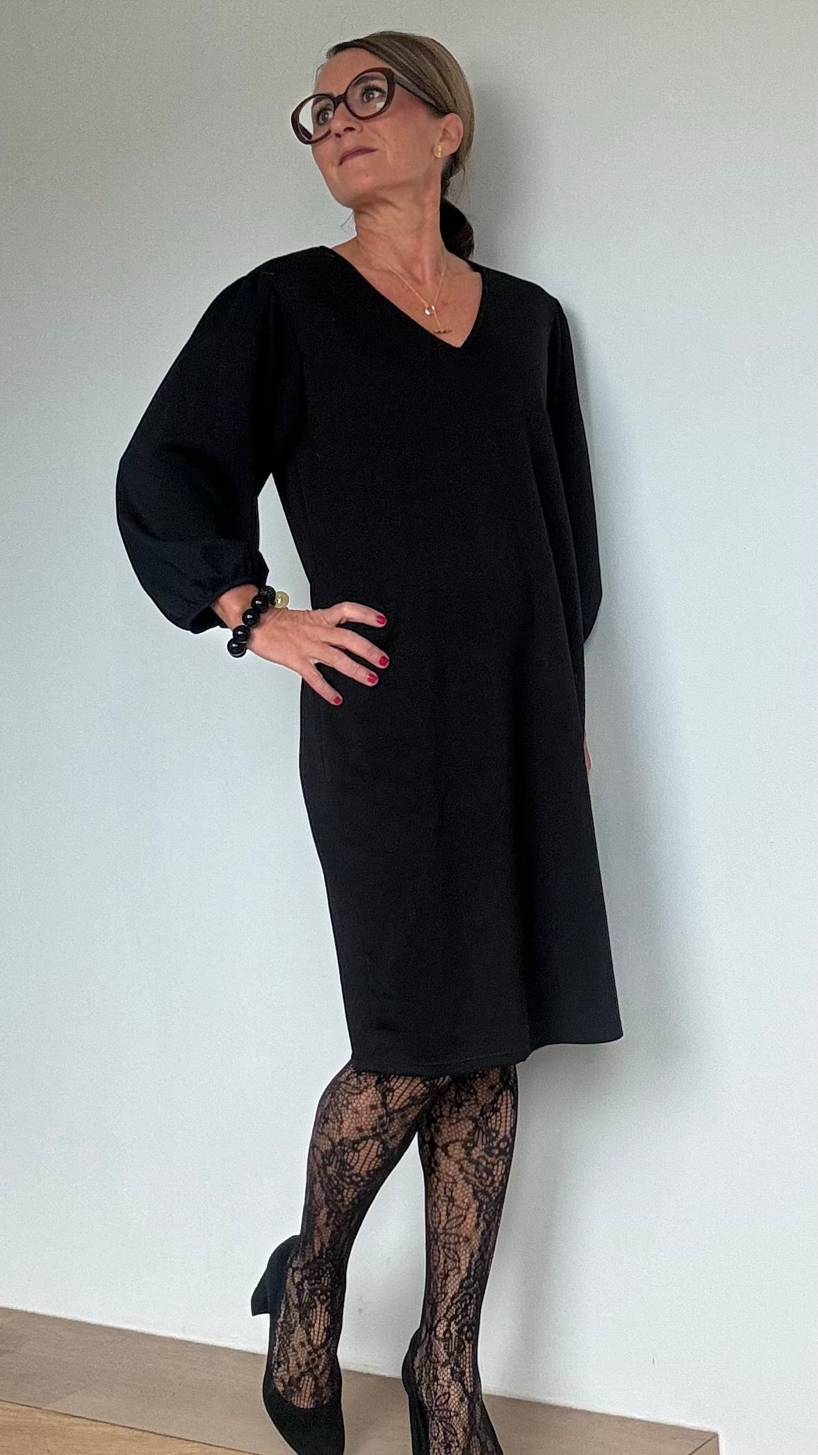 Schwarzes, knielanges Kleid mit V-Ausschnitt und langen Ballonärmeln. Das Kleid hat einen geraden, fließenden Schnitt und besteht aus einer Mischung aus Viskose und Polyester. Es ist schlicht und elegant, perfekt kombinierbar mit Pumps oder Stiefeln für verschiedene Anlässe. Ideal für Frauen mit Kleidergröße 34-40, Länge ca. 94 cm.