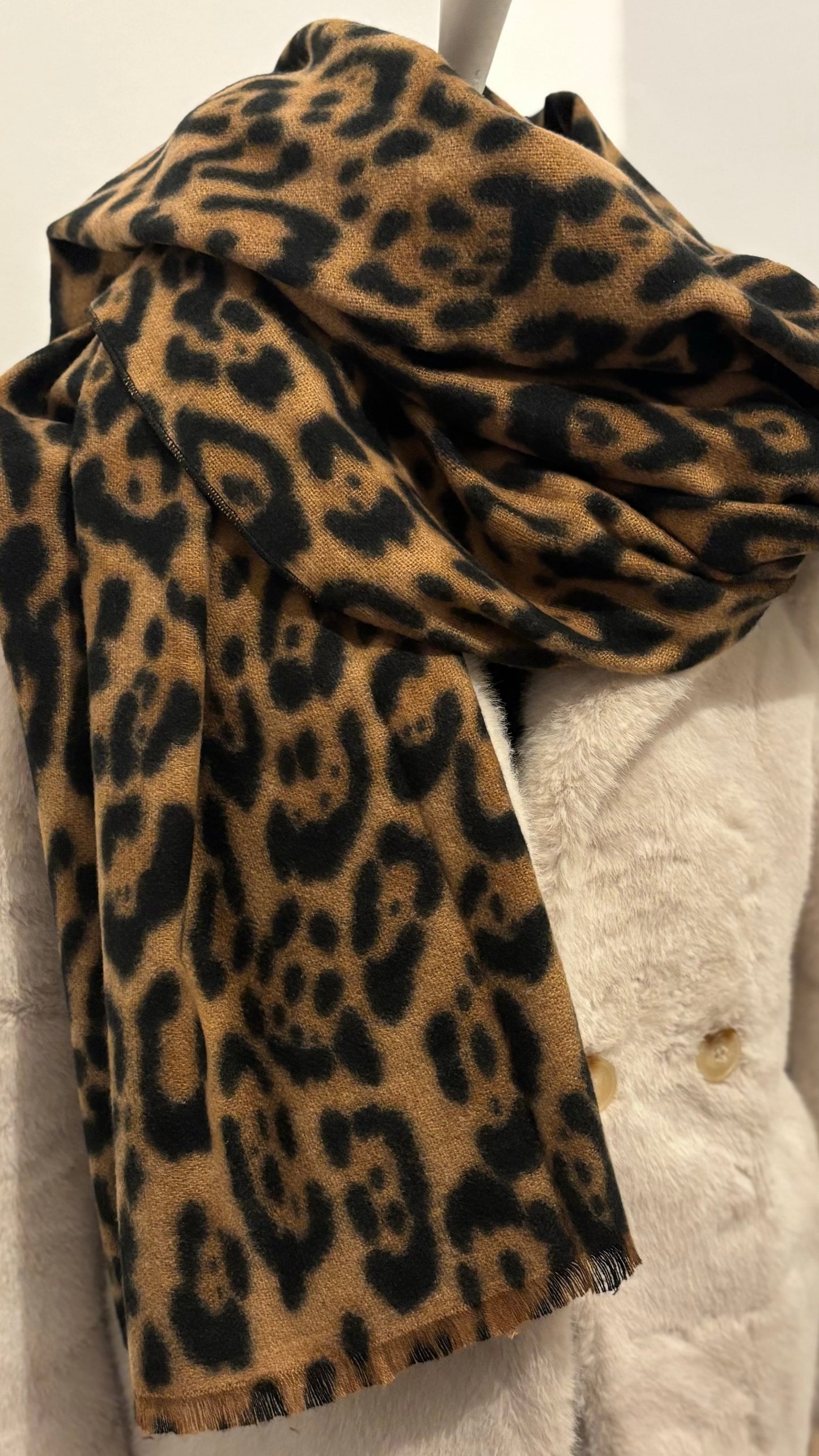 Weicher Schal mit klassischem Leo-Print in warmen Naturtönen. Großformat mit feinen Fransen, locker über einen schwarzen Mantel gelegt. Wirkt edel, cozy und modisch zugleich.