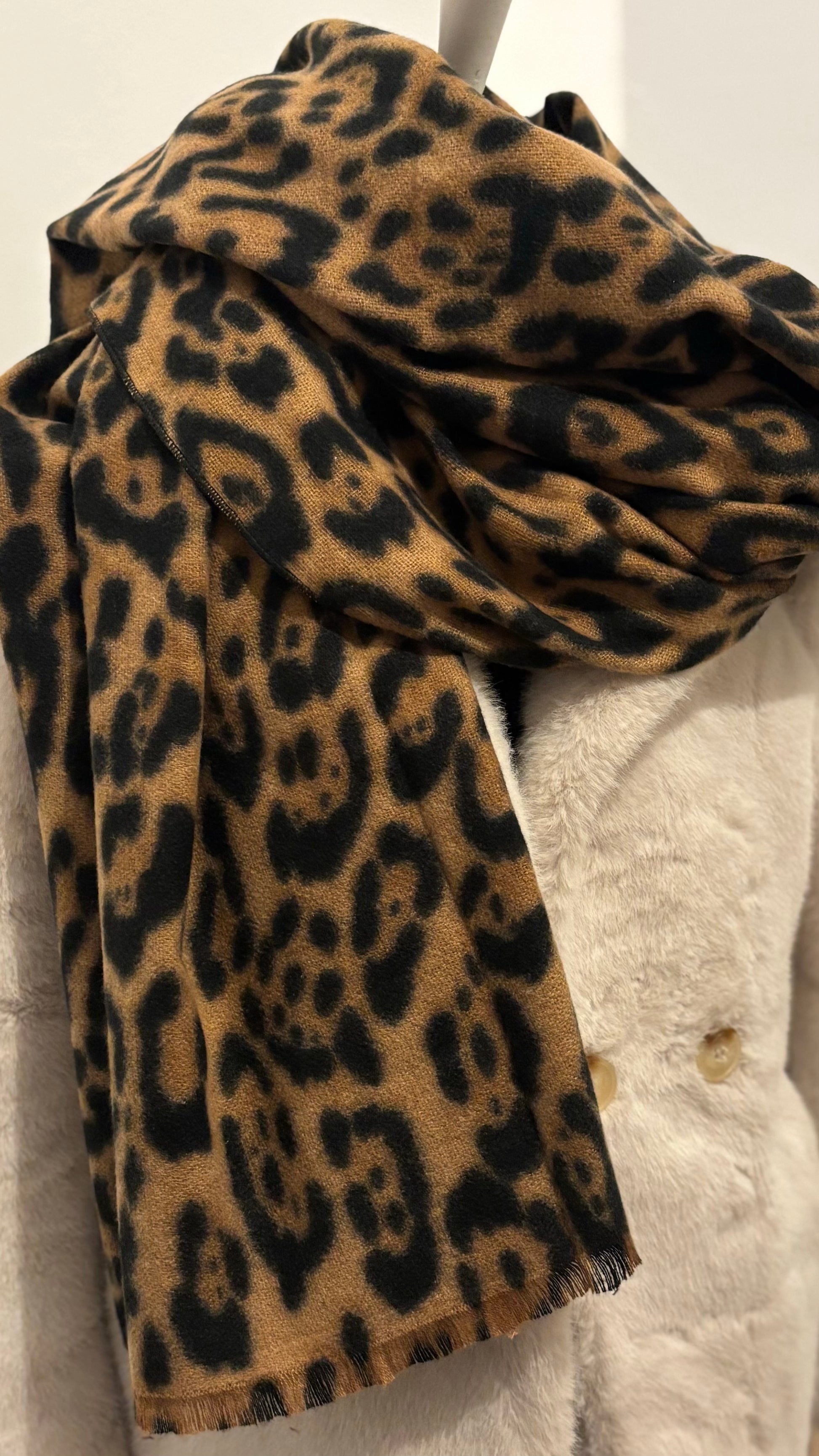 Weicher Schal mit klassischem Leo-Print in warmen Naturtönen. Großformat mit feinen Fransen, locker über einen schwarzen Mantel gelegt. Wirkt edel, cozy und modisch zugleich.