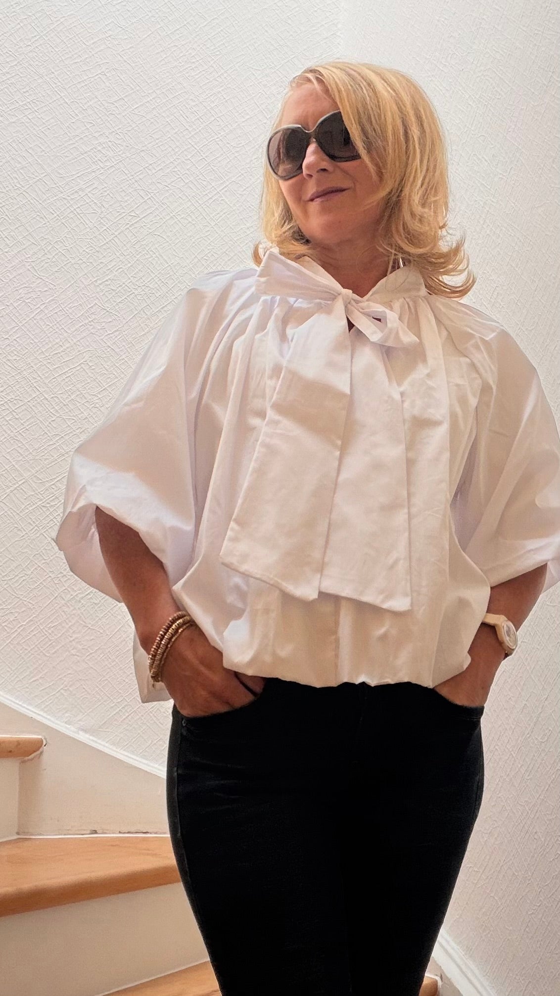 Miss Lotti  trägt eine weiße Ballonbluse mit weiten 3/4-Ärmeln, gerafftem Saum und Bindeschleife am kleinen Stehkragen.