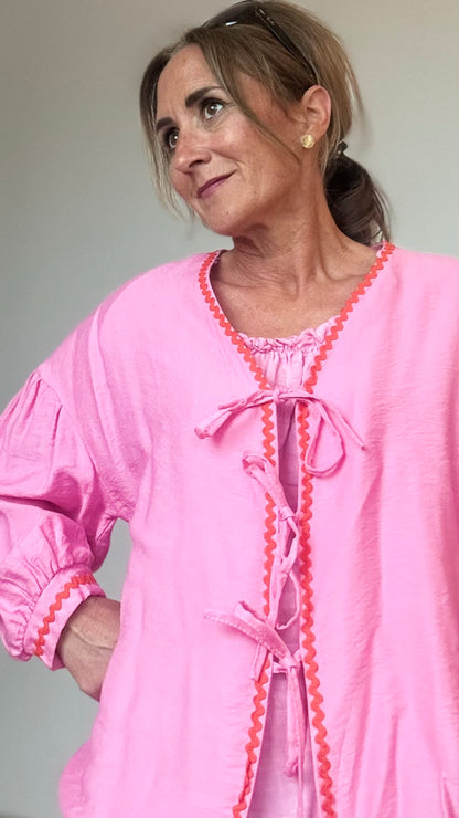 Blusen-Jäckchen aus pinkfarbener Viskose mit orangefarbener Zierkante, leichtem Puffärmel, überschnittenen Schultern und Bindebändern vorn. Rückenlänge 62 cm, locker geschnitten, vielseitig kombinierbar von Größe 34–40.