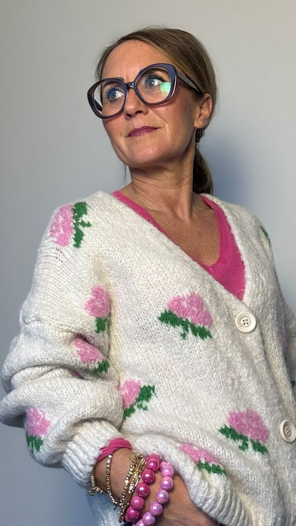 Kuschelig weicher Strickcardigan mit V-Ausschnitt, Knopfleiste und romantischen eingestrickten Blumen in Rosa. Ballonärmel mit schmalem Bündchen. Erhältlich in Schwarz und Wollweiß, passt von Größe 34 bis 40. Perfekt für stilvolle Layering-Looks in der Übergangszeit.