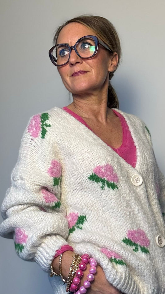 Kuschelig weicher Strickcardigan mit V-Ausschnitt, Knopfleiste und romantischen eingestrickten Blumen in Rosa. Ballonärmel mit schmalem Bündchen. Erhältlich in Schwarz und Wollweiß, passt von Größe 34 bis 40. Perfekt für stilvolle Layering-Looks in der Übergangszeit.