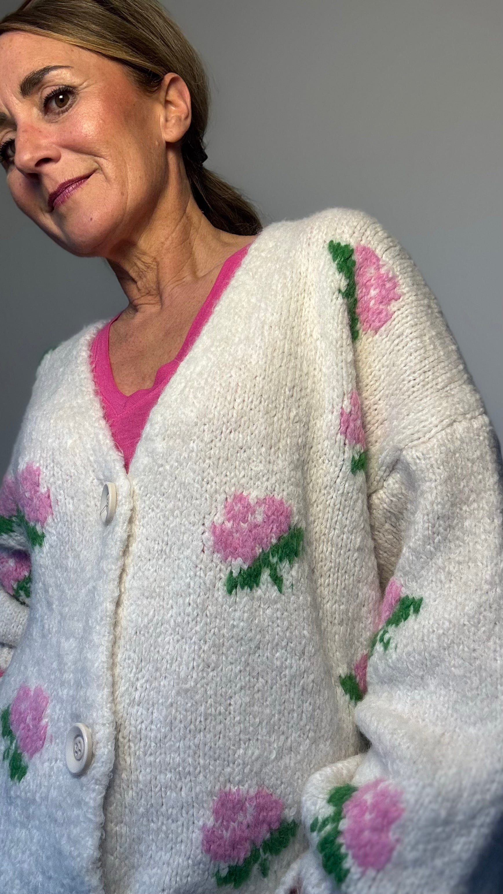 Kuschelig weicher Strickcardigan mit V-Ausschnitt, Knopfleiste und romantischen eingestrickten Blumen in Rosa. Ballonärmel mit schmalem Bündchen. Erhältlich in Schwarz und Wollweiß, passt von Größe 34 bis 40. Perfekt für stilvolle Layering-Looks in der Übergangszeit.